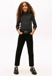 Schwarz-weiß gestreiftes Rollkragenoberteil kombiniert mit schwarzen Hosen und schwarzen Loafers, ausgestattet mit einem Gürtel und geschlossenem Design.