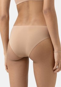 Intimo beige senza cuciture con una superficie liscia, taglio a vita media e cinturino elastico minimale, mostrato da dietro.