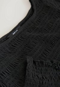 Gros plan sur un tissu noir froncé sur un haut sans manches avec un col carré et un petit détail de bordure à volants.