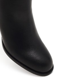 Bottine en cuir noir à bout rond, texture lisse, design minimaliste et semelle noire légèrement surélevée.