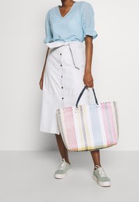 Torebka plażowa w wielokolorowym splocie z niebieskimi i białymi paskami, z mocnym ciemnym uchwytem. Połączona z jasnoniebieską bluzką i białą spódnicą.