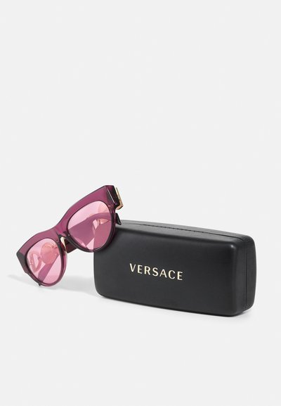 Ochelari de soare Versace cu forma cat-eye, rame de culoare mov închis, lentile roz gradient și un capac de protecție negru cu logo auriu.