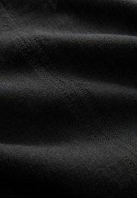 Gros plan d'un tissu noir montrant une double couture détaillée et un motif de tissage texturé.