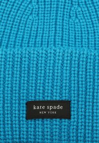 Dzianinowa niebieska czapka beanie o ryflowanej fakturze, z czarną metką z białym napisem "kate spade NEW YORK" wyszytym na dole.