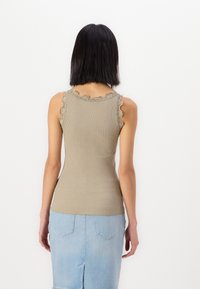 Ribbet tanktopp i dempet olivengrønn med bølget blondedetalj ved skuldrene. Tett design som passer godt med et lyst denimskjørt.