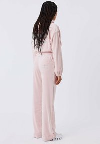 Roze velours lounge-outfit bestaande uit een cropped pullover en wijde broek met een elastische tailleband en detail van een achterzak.