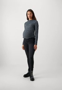 Grå långärmad topp med strukturerat mönster, kombinerad med svarta smala jeans och svarta ankelboots. Outfiten har en slimmad, figursydd silhuett.