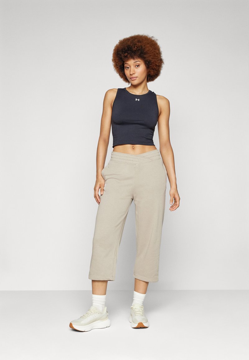 Schwarzes, kurzes Tanktop und weite, hellbeige Sweatpants. Das Modell trägt weiße Sneaker und weiße Socken und steht vor einem neutralen Hintergrund.