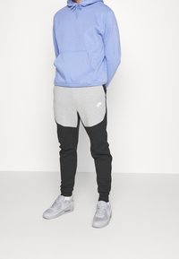 Ljusblå hoodies med ficka fram, kombinerad med grå och svarta färgblockerade mjukisbyxor. Grå Nike-logga på byxorna, bärs med grå sneakers.