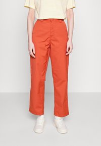Heldere oranje wijde broek met een zachte textuur, hoge taille en sluiting met een knoop aan de voorkant, in combinatie met witte sneakers.