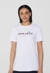 Bílá bavlněná tričko s nápisem "BONJOUR" a grafikou srdce a třešně. Krátké rukávy, kulatý výstřih, uvolněný střih.