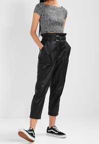Pantalones cortos de imitación de cuero negro con cintura alta y detalle de cinturón, combinados con un top de punto ajustado a rayas negras y blancas, y zapatillas negras.