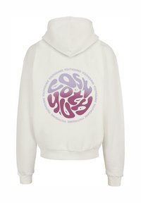 Sudadera blanca con un gran gráfico circular en la parte trasera, que presenta la palabra "YOUTHQUAKE" en tonos morados, con un diseño de texto redondeado y puños acanalados.