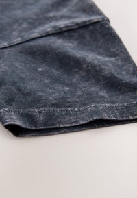 Denim stof in donkerblauw met een versleten textuur, met een opgerolde zoom en zichtbare stiksels, gepresenteerd onder een hoek.