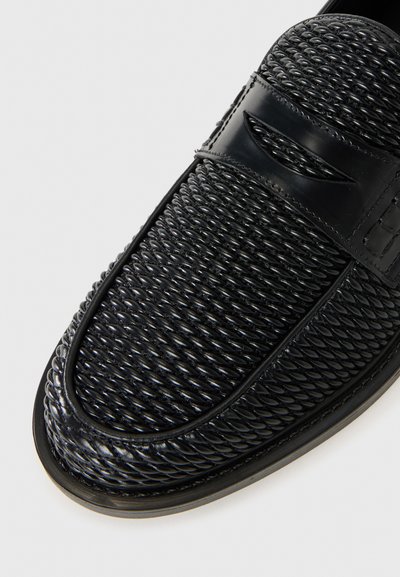 Schwarze Lederloafers mit gewebter Textur im oberen Bereich, glattem Zehenbereich und glänzender Oberfläche. Verfügt über eine kontrastierende Gummisohle und ein schlichtes Design.