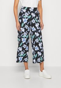 Pantalons larges noirs ornés d'un motif floral bleu et blanc, avec des feuilles vertes. Fabriqués en tissu léger, avec une texture lisse.