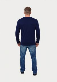 Camicia a maniche lunghe blu navy in un morbido tessuto testurizzato con colletto a girocollo, abbinata a jeans in denim azzurro chiaro e scarpe nere.