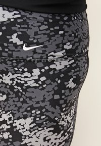 Czarne i szare legginsy w wzory, wykonane z elastycznego materiału, z elastyczną talią i małym białym logo Nike na plecach.