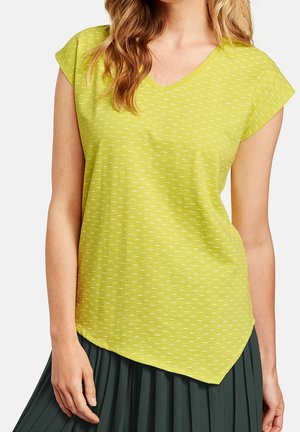 Mujer con una blusa de manga corta en verde lima con escote en V y estampado de rayas blancas, y una falda oscura plisada.