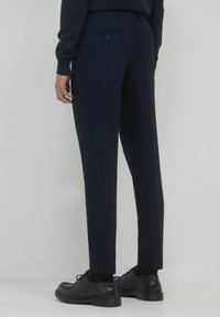 Pantaloni navy con un taglio su misura, caratterizzati da una texture liscia, gambe affusolate, tasche posteriori e scarpe in pelle nere per un contrasto.