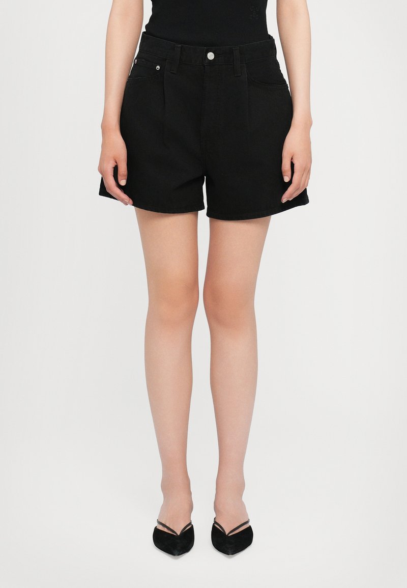Les shorts en denim noir présentent un design taille haute, un style classique à cinq poches et un ourlet qui tombe au-dessus du genou. Texture lisse sur l'ensemble.