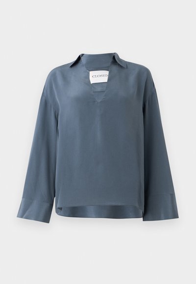 Pikkade varrukatega sinine satiinist pluus, millel on V-kaelus ja krae. Omab kastikujulist lõiget ja siledat tekstuuri käistest. Brändi silt on nähtav seest.