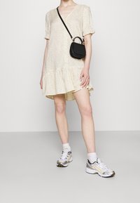 Abito color crema con maniche corte, motivo a pois e orlo arricciato. Abbinato a sneakers bianche e una piccola borsa nera.