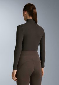 Barna, hosszú ujjú felső, magas gallérral, sima textúrával, magas derekú, hozzá illő leggingsszel párosítva. Egyszerű, testhezálló dizájn.