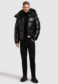Black puffer jacket with a shiny finish, featuring a large hood, zip closure, and side pockets, paired with black pants and boots.