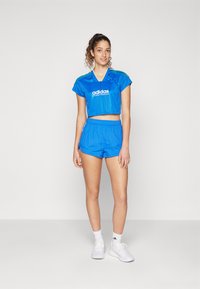 Zila adidas sporta apģērba komplekts, kas sastāv no īsā tops un atbilstošām šortiem. Audums ir gluds ar spīdīgu apdari. Ietver logotipa detaļu.