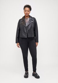 Black leather biker jacket with silver hardware, zippered front, and wide collar; paired with black skinny jeans and shiny platform shoes.