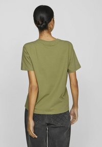 Olivgrön kortärmad t-shirt i bomull, med rund halsringning och avslappnad passform, kombinerad med mörkgrå byxor som har kviltade fickor.