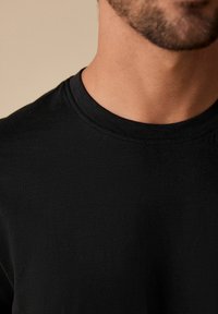 Camiseta negra de cuello redondo, hecha de una tela suave y texturizada. Presenta un neckline acanalado y un diseño ajustado. Sin patrones ni acentos visibles.