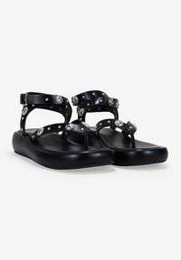 Sandalias negras con correa ajustable para el tobillo, con decoración de tachuelas plateadas y diseño de tira entre los dedos. Fabricadas con material de goma suave y flexible.