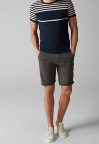 T-shirt à rayures bleu marine et crème à manches courtes associé à un short gris. Le short présente des ourlets retournés et est complété par des sneakers claires.