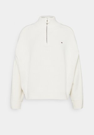 Witte geribbelde gebreide trui met een halve ritssluiting en een klein logo op de linkerbuste, voorzien van lange mouwen en een hoge kraag.