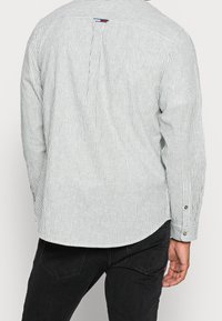 Camisa de manga larga a rayas en verde y blanco, con dobladillo redondeado, puños abotonados y una etiqueta con el logo en la parte posterior del cuello.