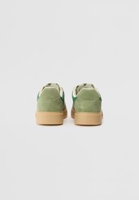 Groene suède sneakers met een gestructureerde rubberen zool, met een laag profiel ontwerp en een subtiele brandingdetail op de hiel.