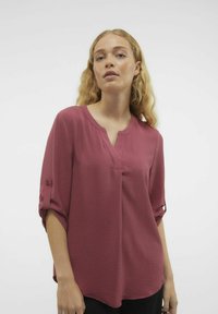 Blusa color lampone con scollatura a V e maniche a tre quarti. Tessuto testurizzato che si drappa delicatamente, con linguette per risvoltare le maniche.