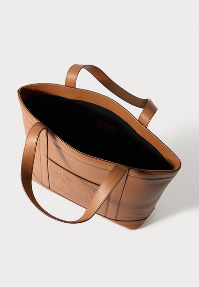 Καφέ δερμάτινη τσάντα ώμου με ανάγλυφο σχέδιο στο μπροστινό μέρος, ανοιχτή κορυφή και δύο στιβαρές λαβές. Το εσωτερικό διαθέτει σκούρο φόδρα.