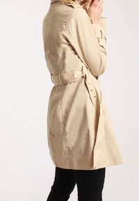 Beige trenchcoat med midjebälte, knappdetaljer och en avslappnad passform. Tillverkad av lätt tyg, med klassisk krage och sidoflikar.