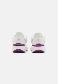 Baskets de sport blanches avec accents roses, dessus en mesh texturé, col rembourré et semelle en caoutchouc violette avec motif de traction.