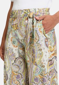 Lehké kalhoty s potiskem mají zavazovací pás, boční kapsy a pastelové barvy s paisley vzory v zelené, fialové a oranžové.