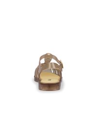 Przezroczyste brązowe sandały z niskim obcasem, z wieloma paskami i boczną klamrą. Podeszwa jest żółta i teksturowana.