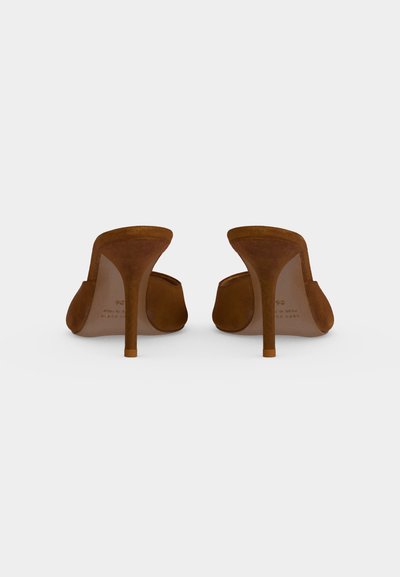 Paire de mules en daim marron à talons hauts montrée de dos avec des talons fins et effilés sur un fond gris clair uni.
