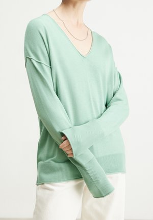 Pull en tricot oversize vert menthe avec un col en V, des poignets et un ourlet côtelés. Texture douce, coupe décontractée et détail de couture subtil.