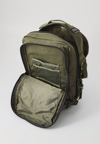 Zaino in nylon verde oliva con chiusura a zip, dotato di una tasca in rete e un ampio interno. Include spallacci regolabili e cuciture rinforzate.