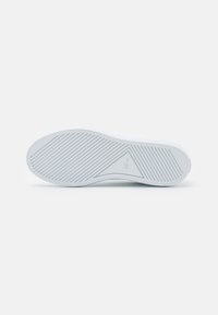 Suola di scarpa in gomma bianca con un motivo testurizzato di linee diagonali e un emblema triangolare. Superficie liscia con una leggera curvatura ai bordi.