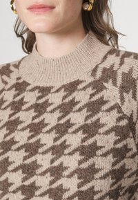 Strickpullover mit Hahnentrittmuster in Braun und Beige. Verfügt über einen hohen gerippten Kragen und Raglanärmel, mit einer weichen Textur.