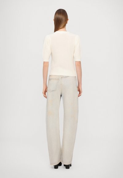 White ribbed knit top with short puff sleeves, paired with light-wash wide-leg jeans featuring faded accents and a classic pocket design.